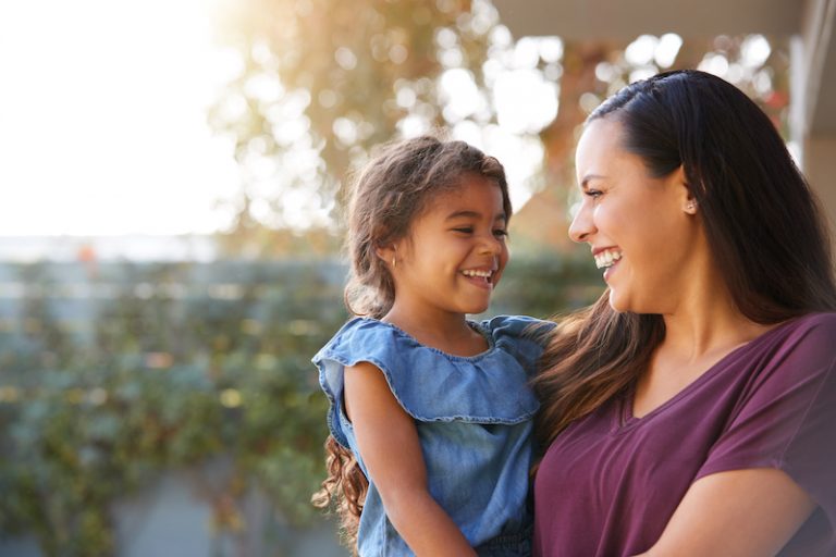 smiling-hispanic-mother-holding-daughter-laughing-in-garden-at-home