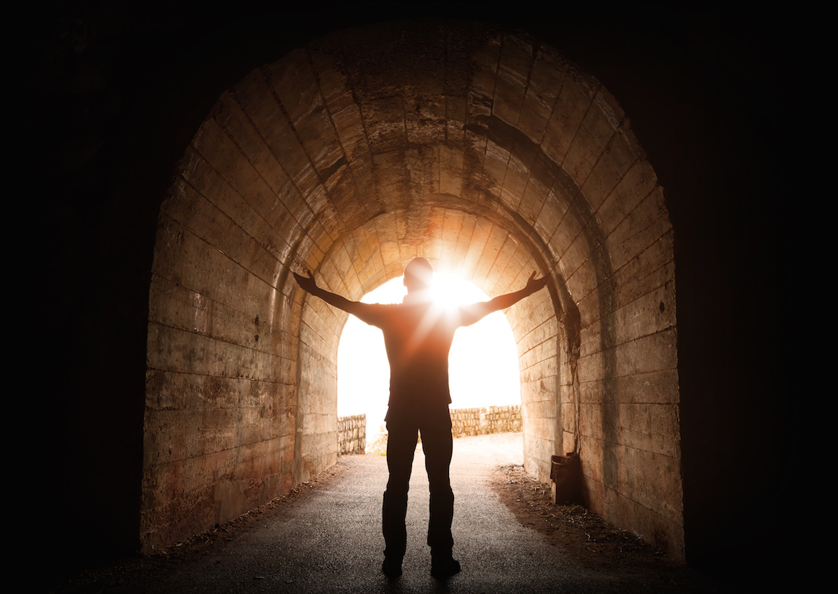 Man stands inside of old dark tunnel with shining sun in the end