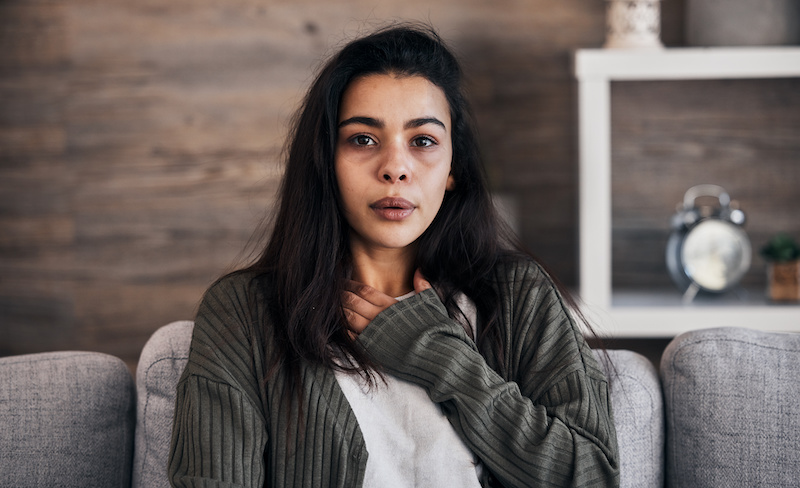 Anxiety worry and woman breathing on sofa to relax calm down and stress relief from panic attack Mental health depression and portrait of anxious girl sitting on couch with hand on chest in pain