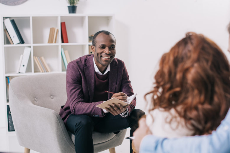 Smiling african american psychiatrist talking to young couple Dr