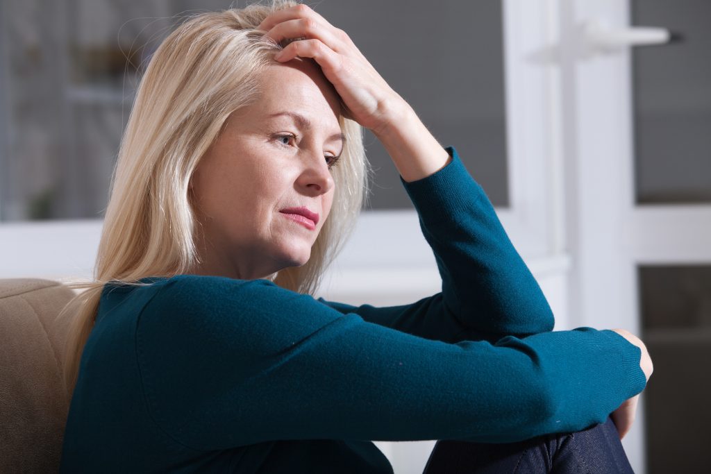 Sad depressed middle aged woman at home sitting on the couch, looking ...